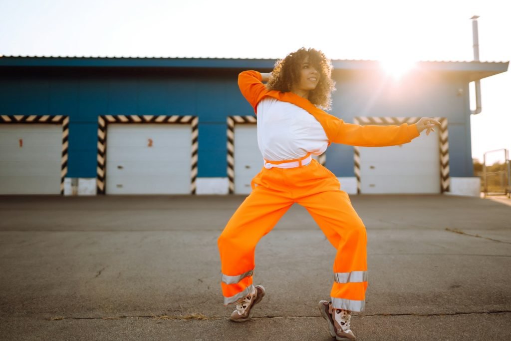 Young African woman - dancer dancing in street at sunset. Stylish woman with curly hair some moves.