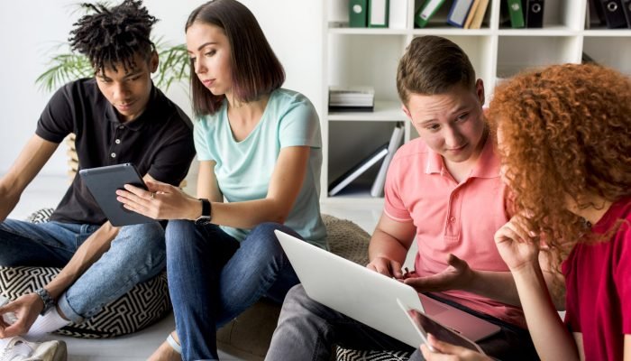 Multiracial Friends Using Electronic Gadgets Sitting Floor Having Discussion